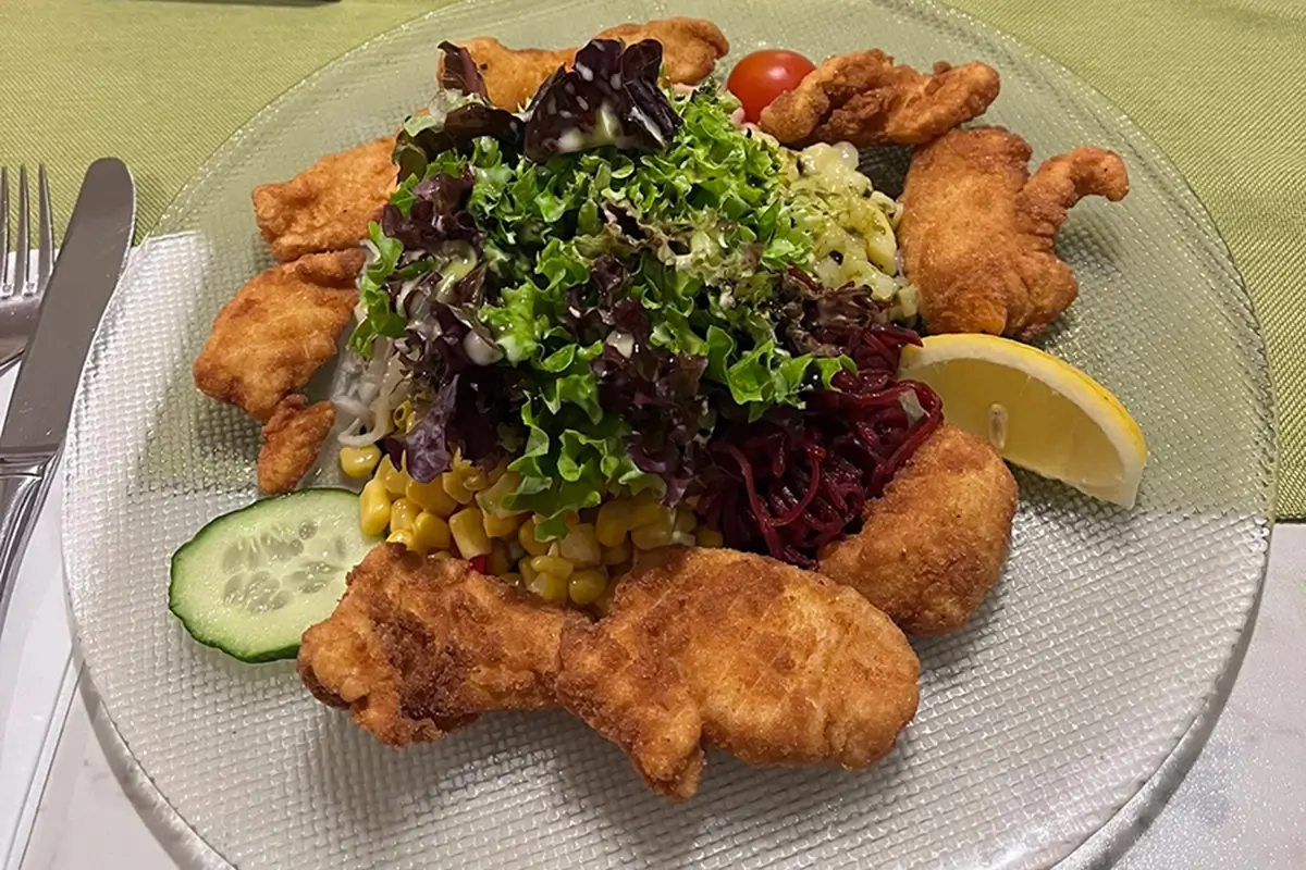 Styrian Backhendl-Salat with crispy fried chicken, fresh lettuce, potatoes, kürbiskernöl (pumpkin seed oil), and salad vegetables.