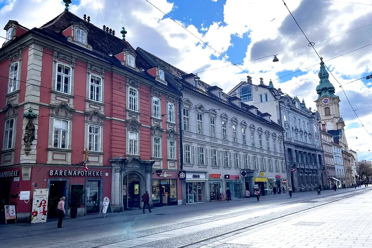 Historic buildings on Herrengasse in Graz with the red Bärenapotheke building on the corner and church in the distance, highlighting things to do in Graz.