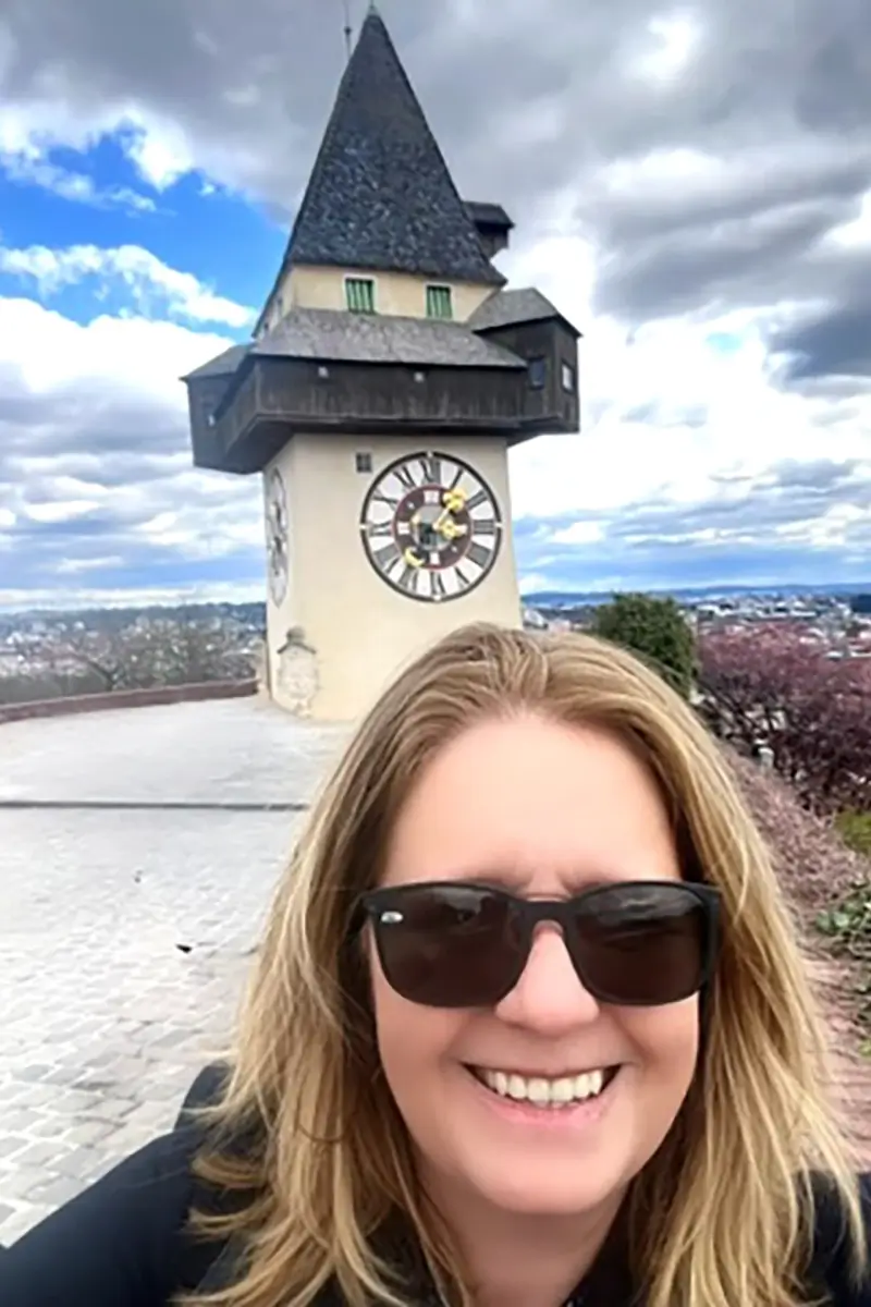 Tammy Ellis, founder of Wanderlustria, on Schlossberg in Graz with the Uhrturm clock tower behind her.
